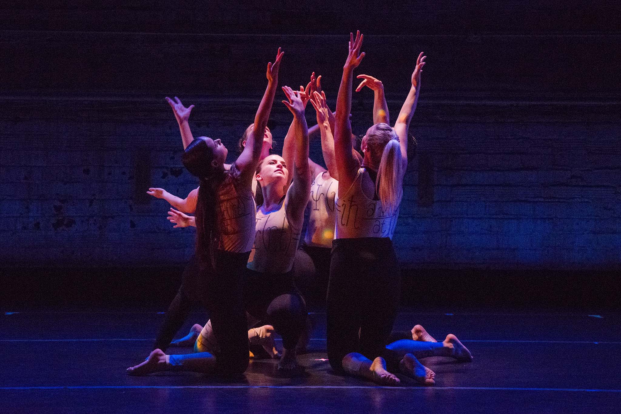 Image of 4 MorrisonDancers huddled together on a black stage for their Quantum Entanglement performance